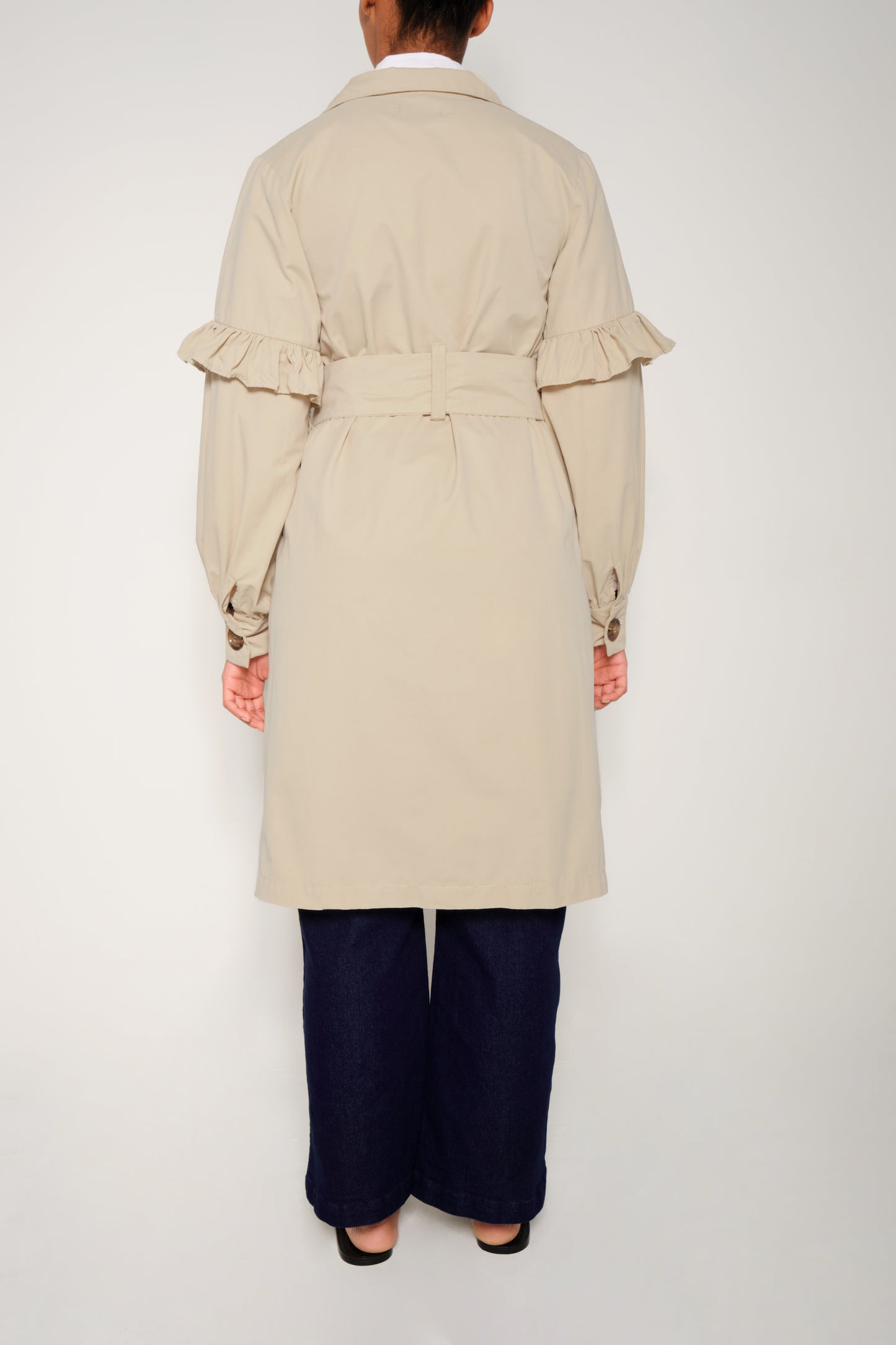 Model wearing women’s ruffle trench coat with belt and volant details