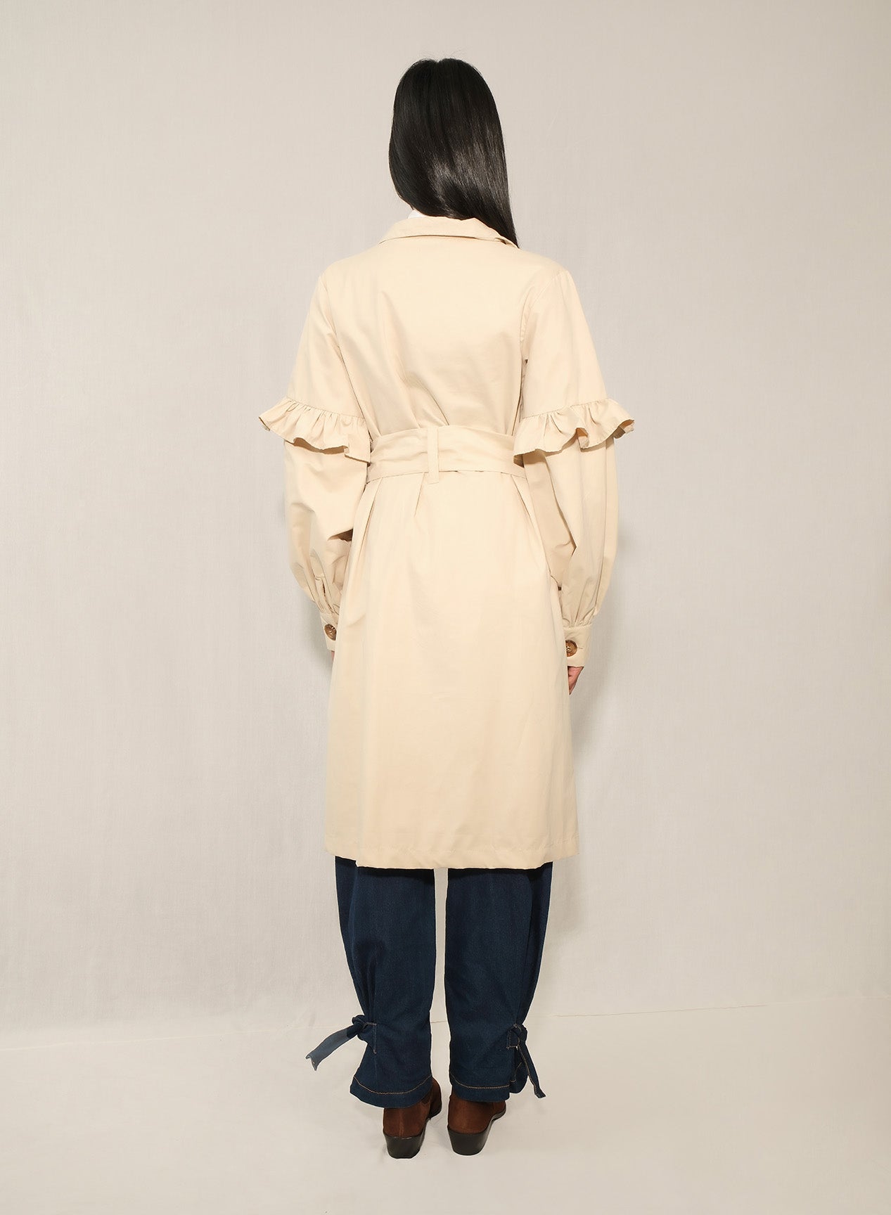 Model wearing women’s ruffle trench coat with belt and volant details
