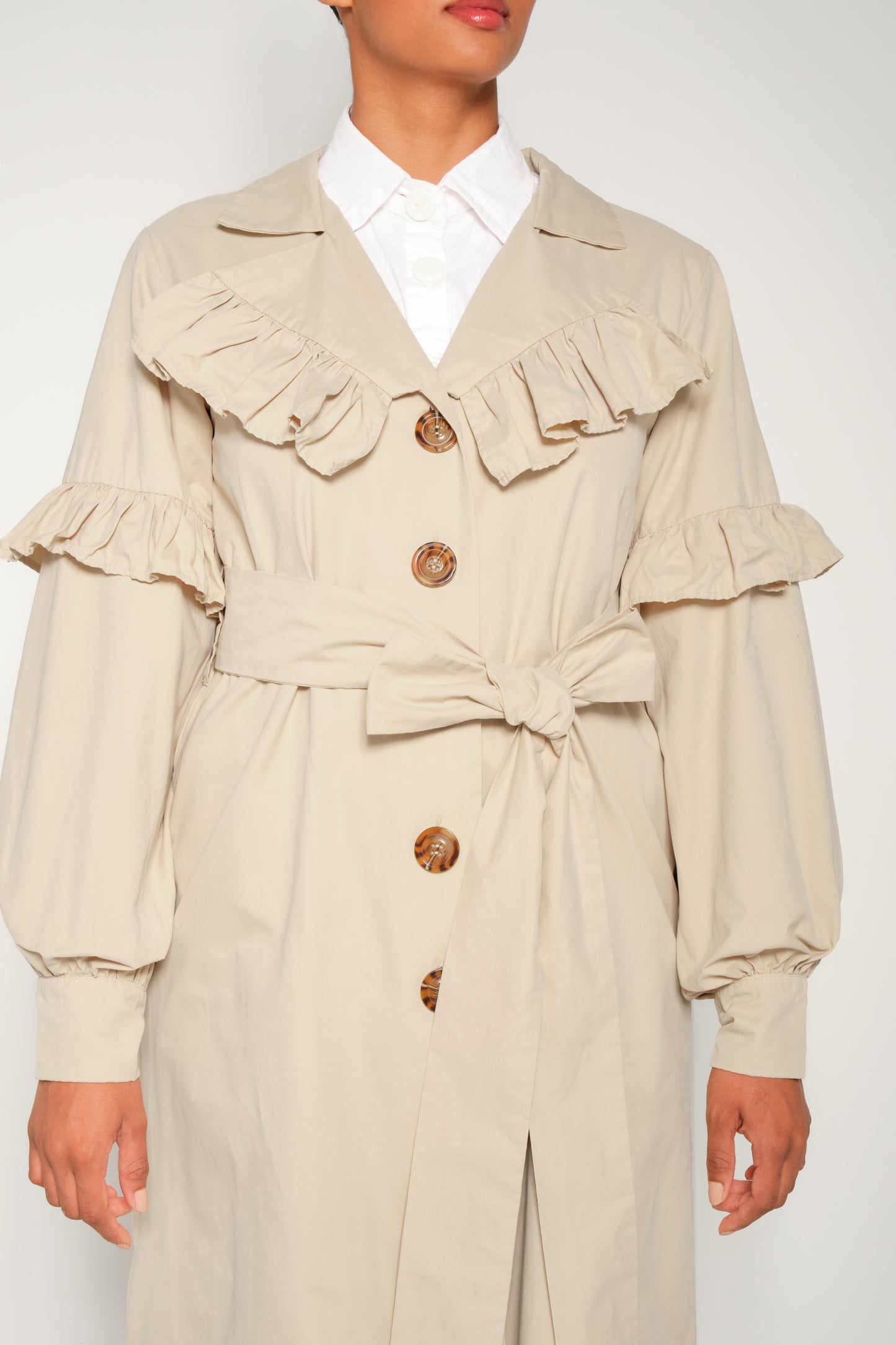 Model wearing women’s ruffle trench coat with belt and volant details