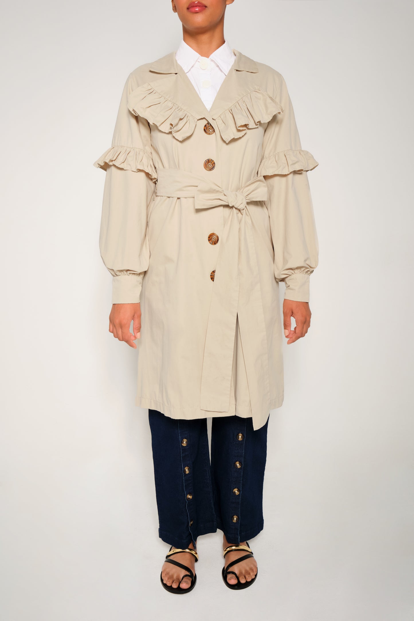 Model wearing women’s ruffle trench coat with belt and volant details