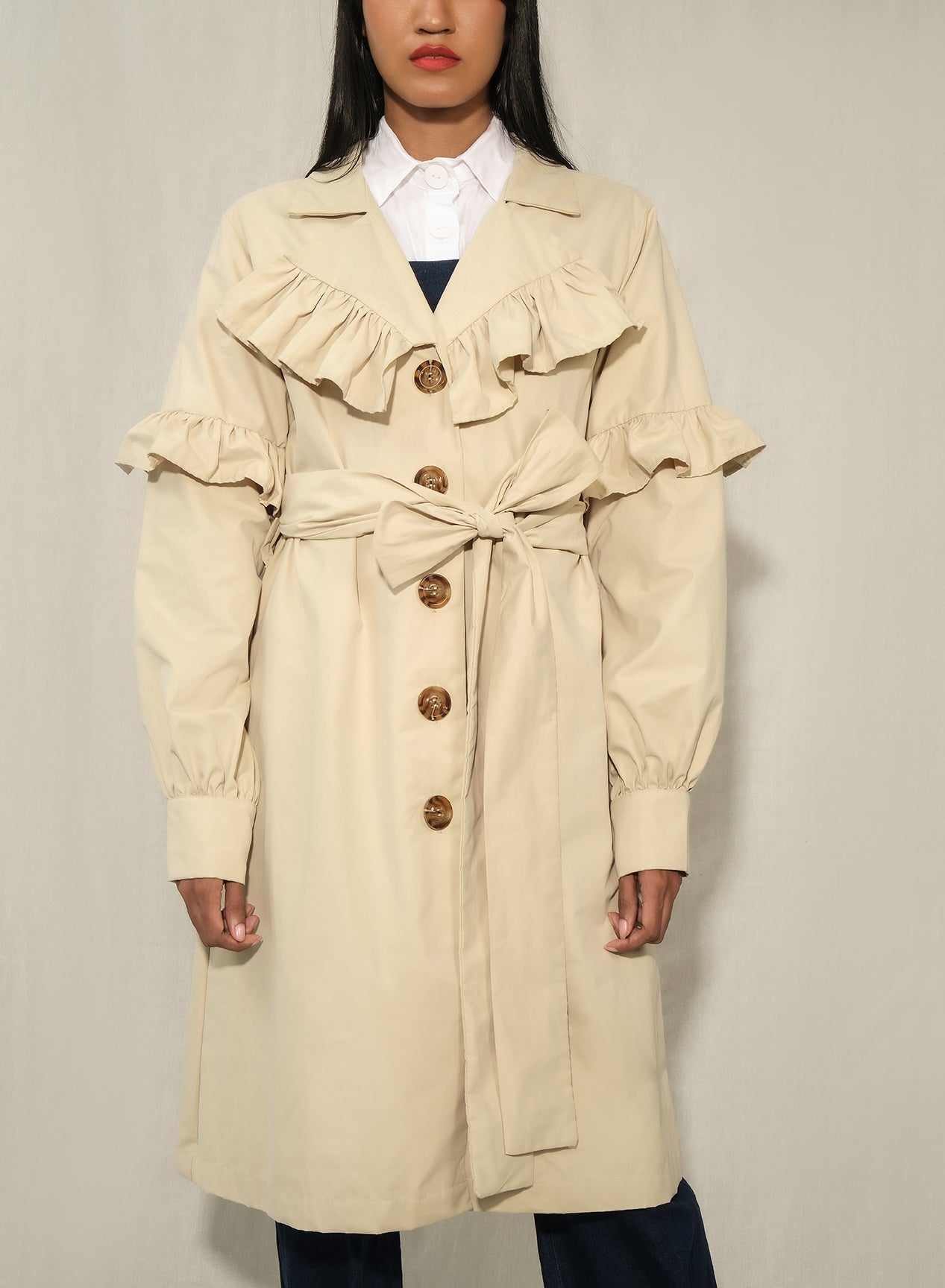 Model wearing women’s ruffle trench coat with belt and volant details