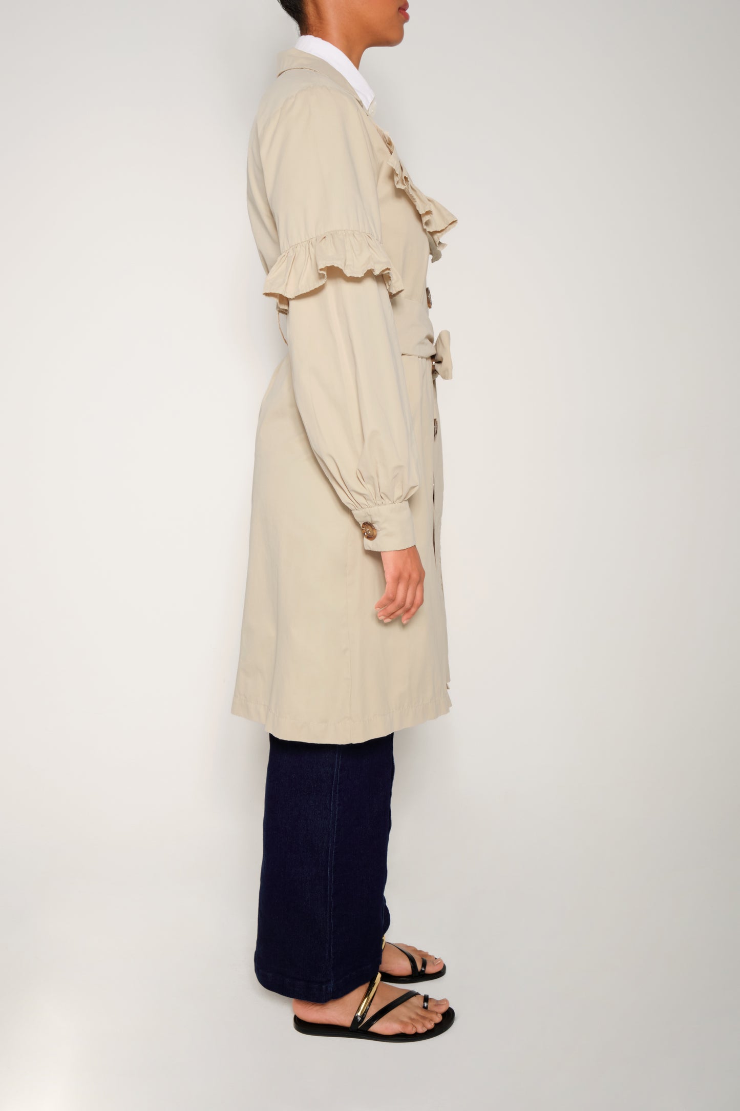 Model wearing women’s ruffle trench coat with belt and volant details