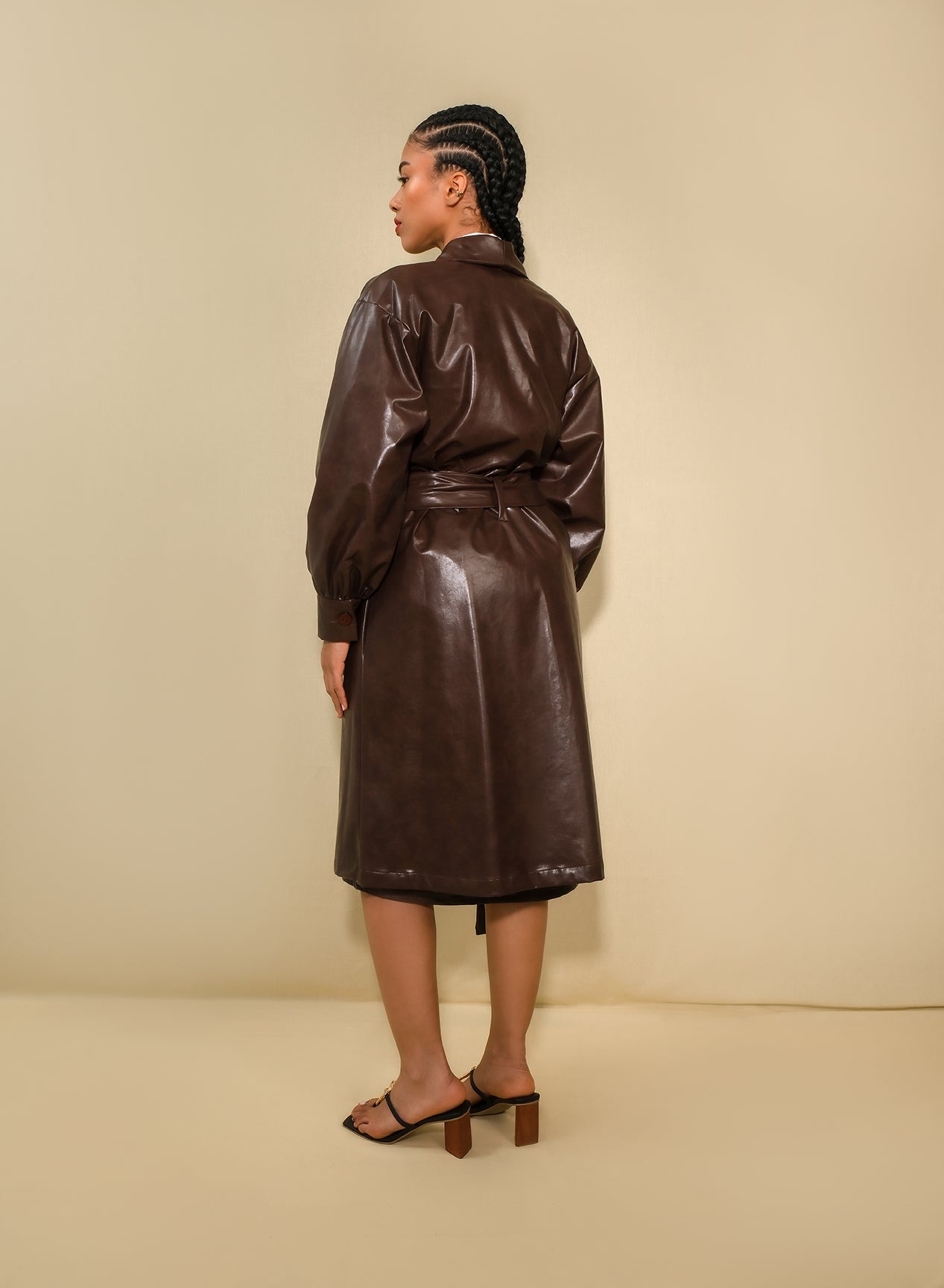 Model wearing chocolate brown faux leather trench coat with belt and puff sleeves.