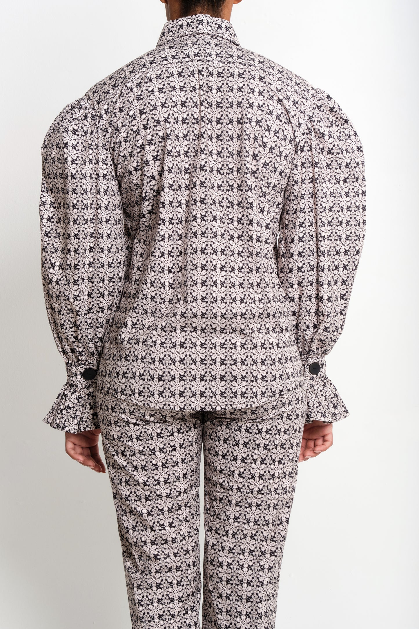 Model in macramé print poplin shirt with puff sleeves and flared ruffle cuffs.