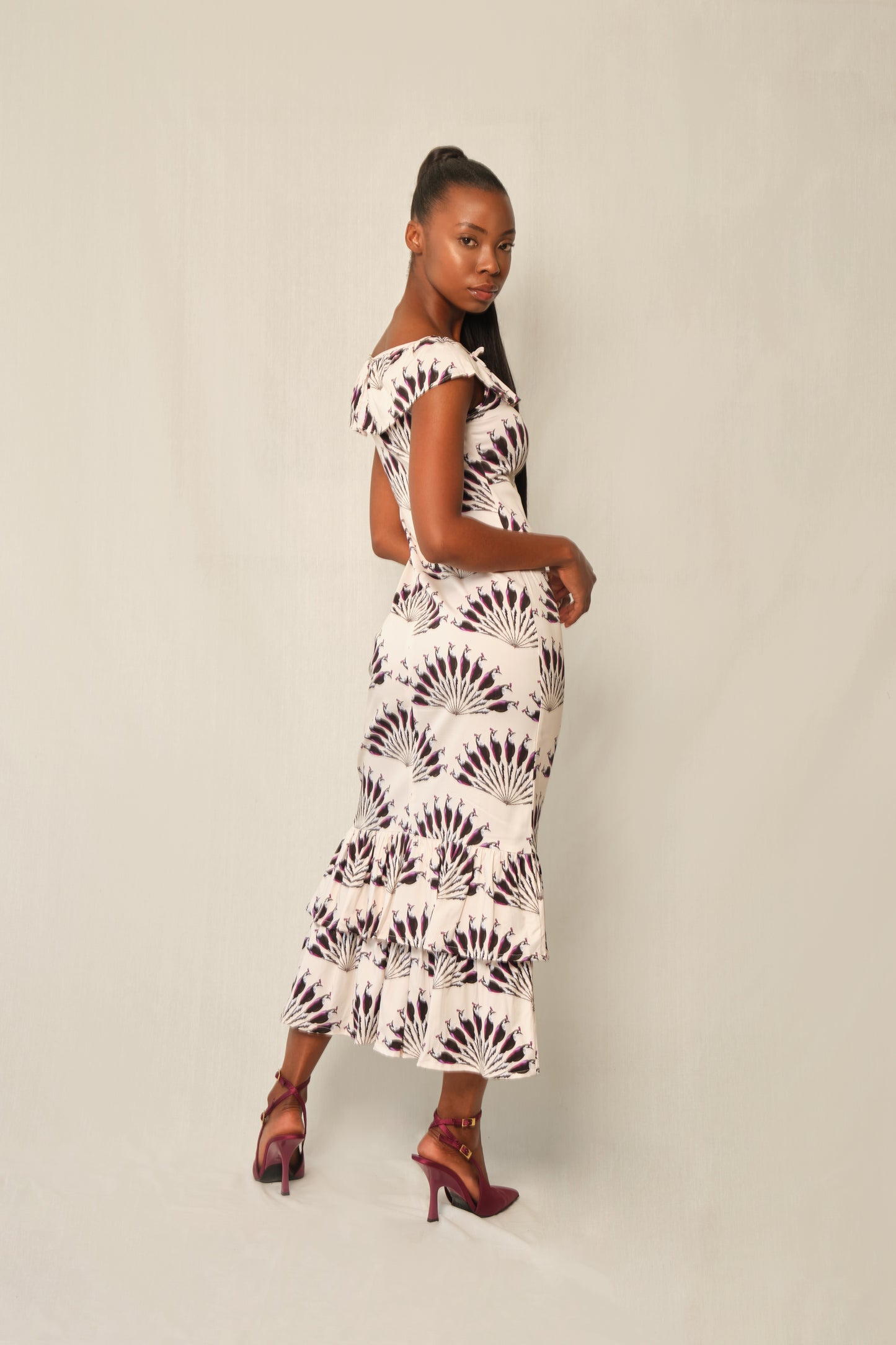 Model wearing fitted viscose midi dress in Throated Ivory print with ruffle neckline, tie keyhole, and double-tier flounce hem
