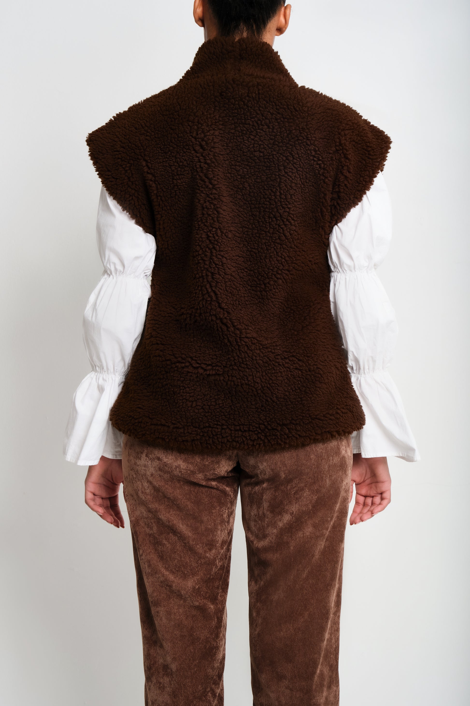 Model wearing brown faux-shearling vest with open front.