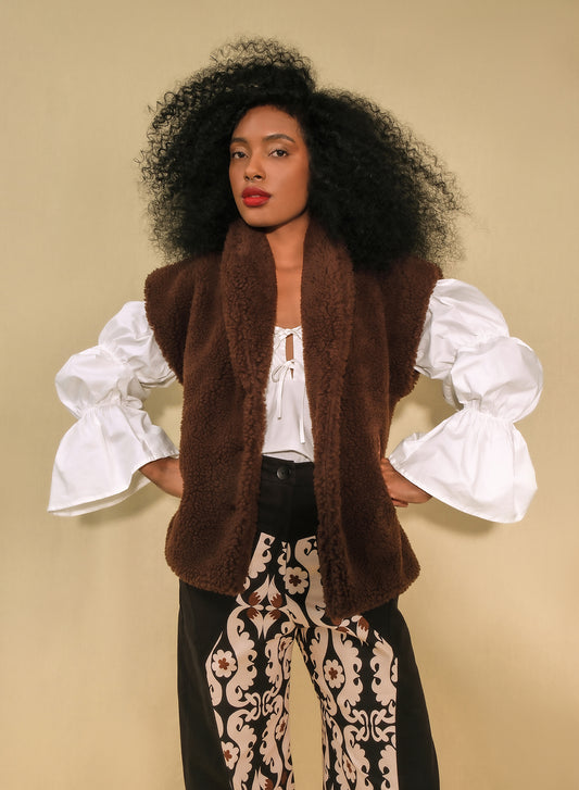 Model wearing brown faux-shearling vest with open front.