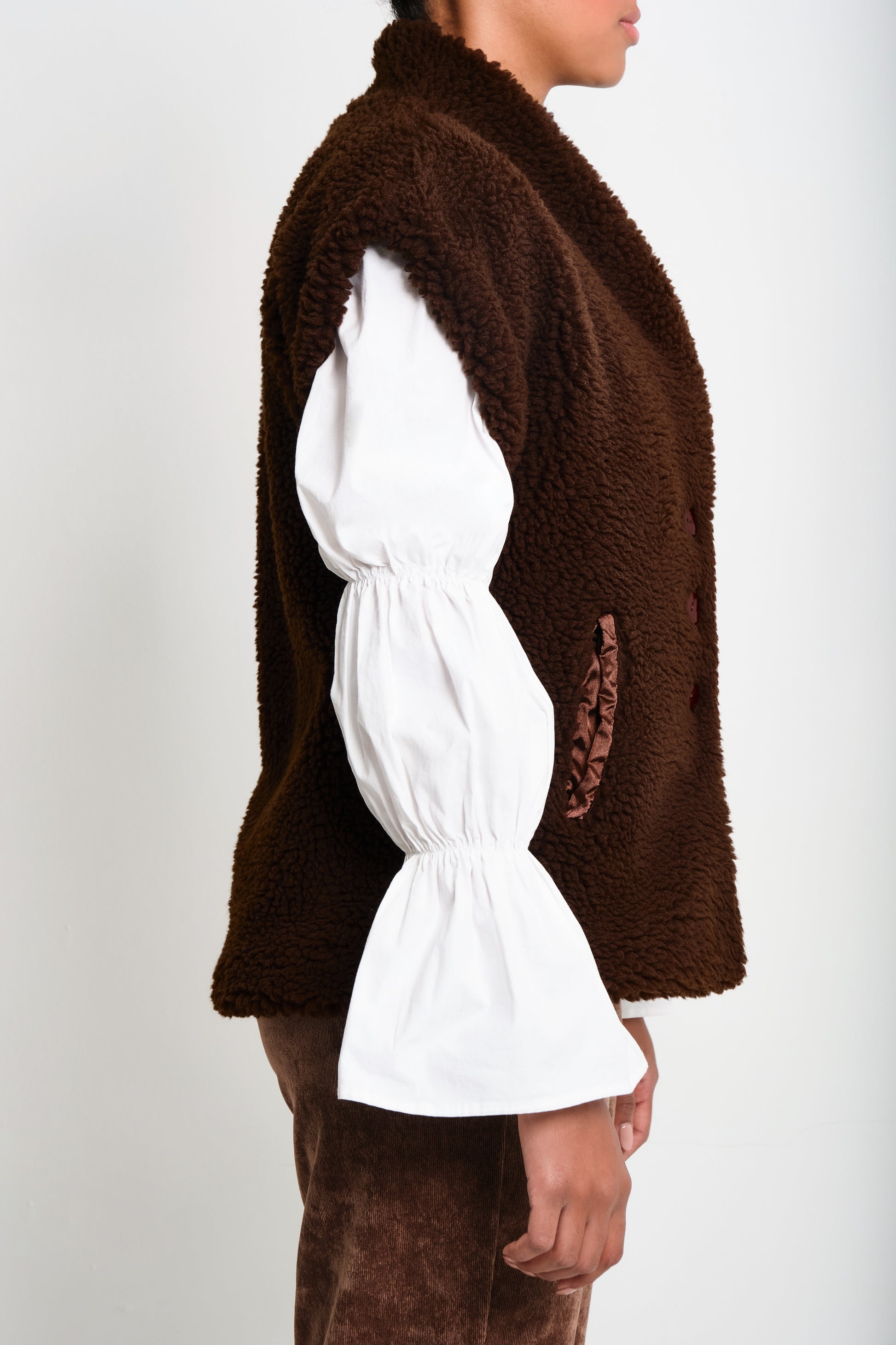 Model wearing brown faux-shearling vest with open front.