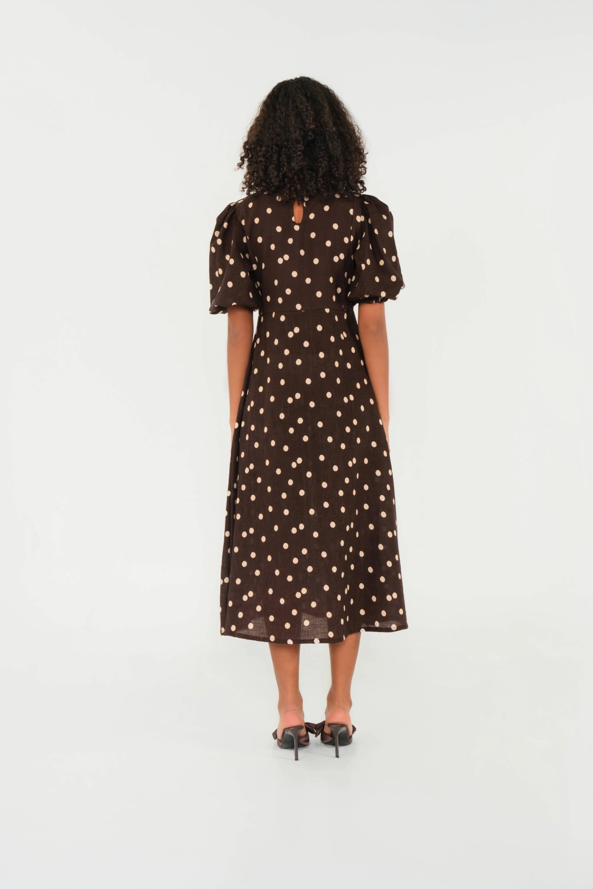Woman wearing a brown dress with white polka dots on a white background