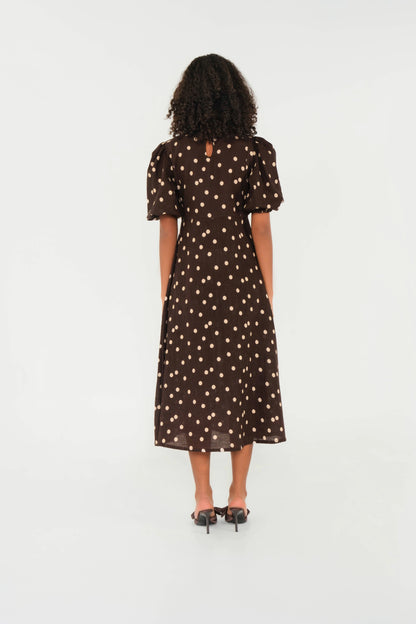 Woman wearing a brown dress with white polka dots on a white background