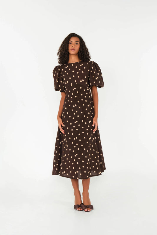 Woman wearing a brown dress with white polka dots on a white background