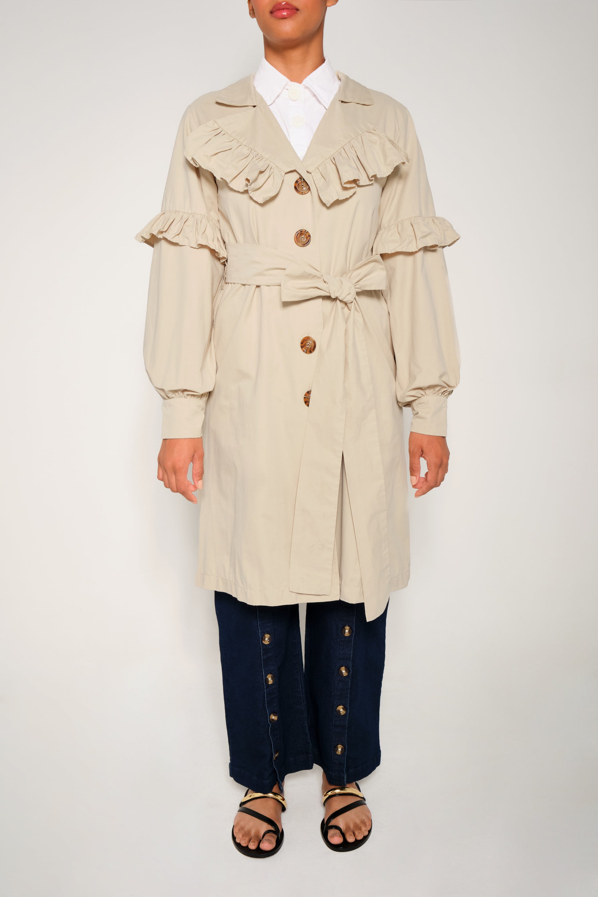 Model wearing women’s ruffle trench coat with belt and volant details