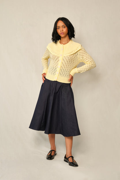 Model wearing indigo A-line denim panel midi skirt with vertical topstitch seams.