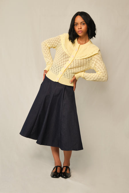 Model wearing indigo A-line denim panel midi skirt with vertical topstitch seams.