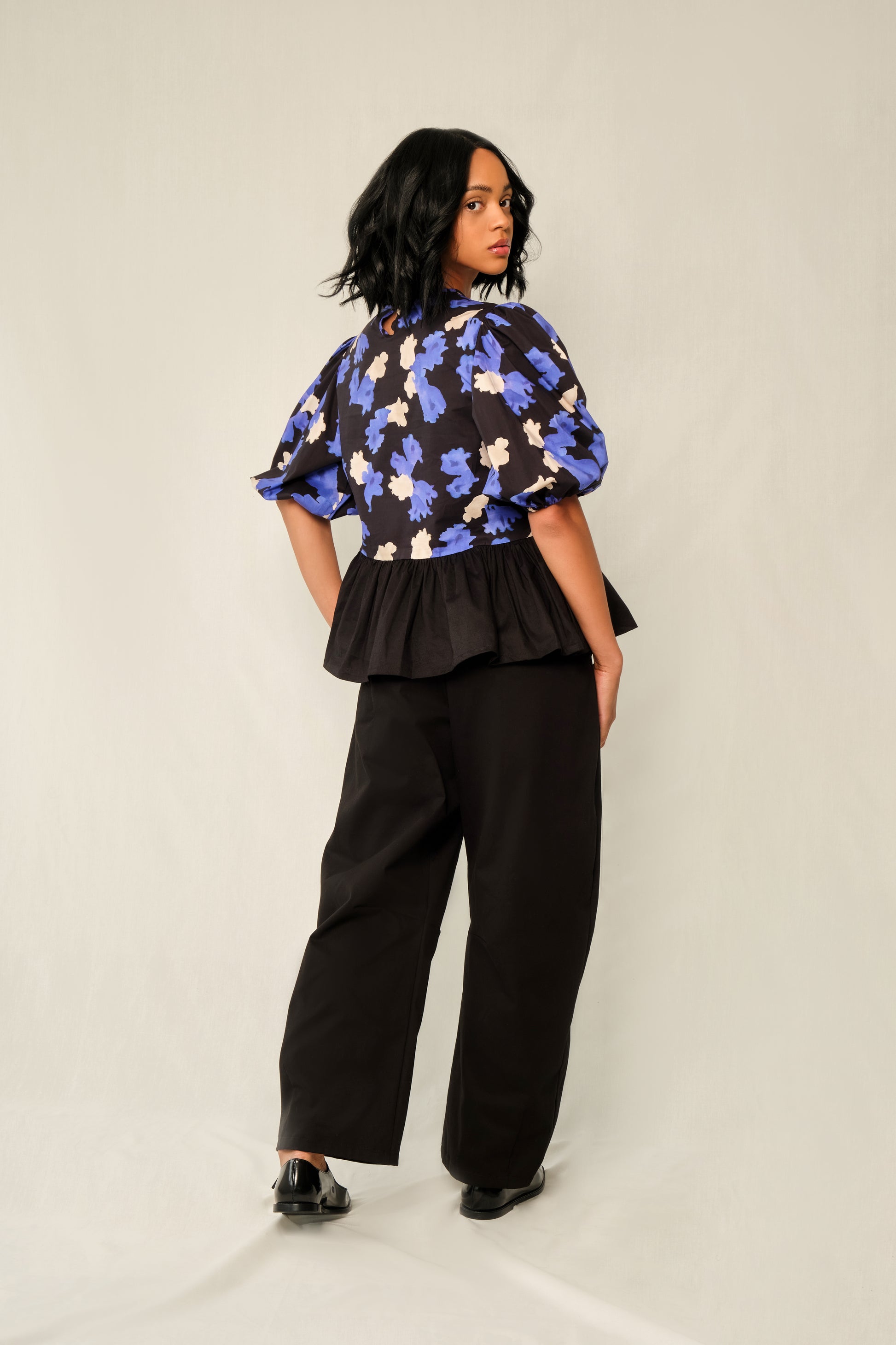 Model wearing puff-sleeve peplum top in Jacaranda print with black poplin peplum and elastic cuffs.