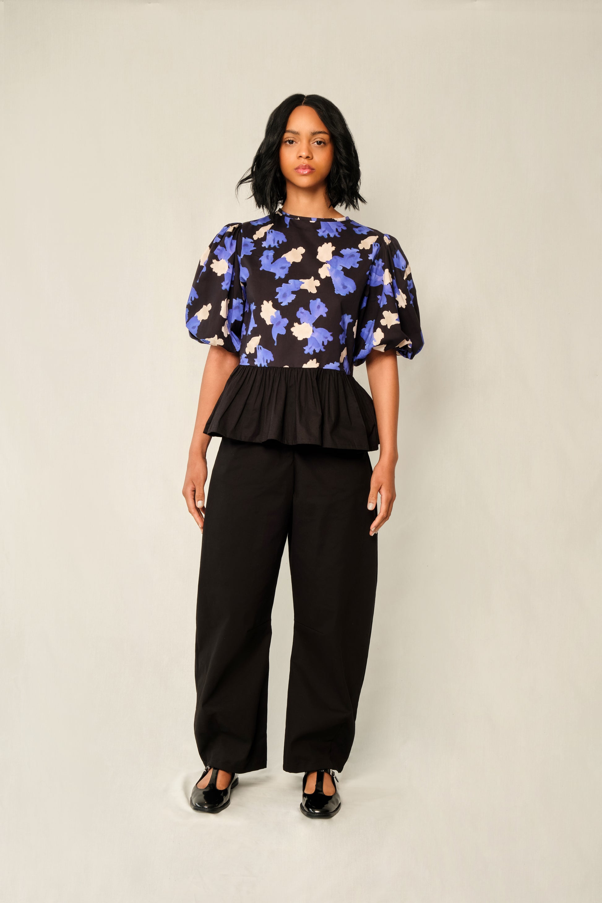 Model wearing puff-sleeve peplum top in Jacaranda print with black poplin peplum and elastic cuffs.