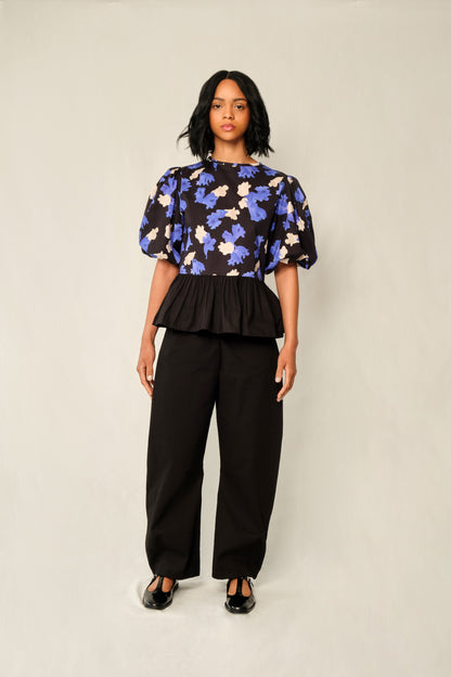 Model wearing puff-sleeve peplum top in Jacaranda print with black poplin peplum and elastic cuffs.