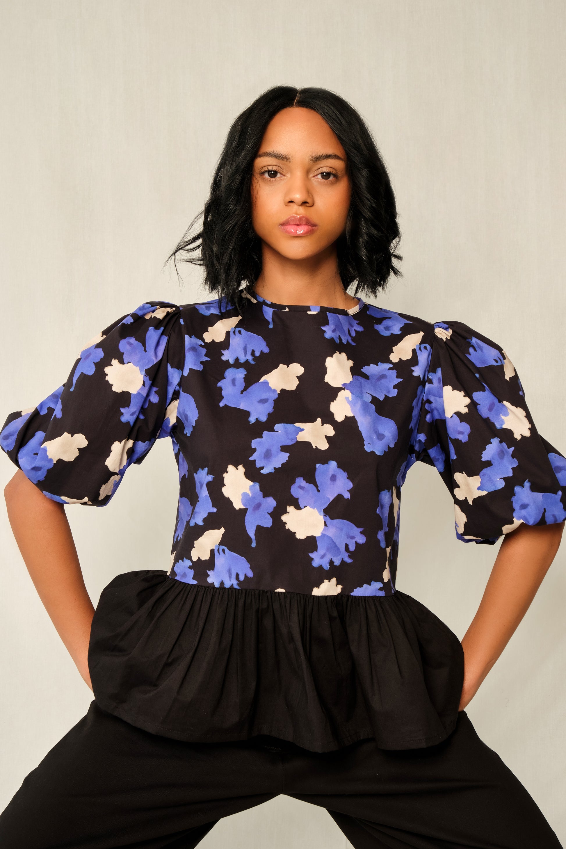 Model wearing puff-sleeve peplum top in Jacaranda print with black poplin peplum and elastic cuffs.