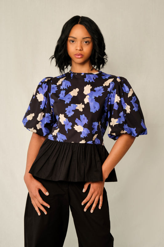 Model wearing puff-sleeve peplum top in Jacaranda print with black poplin peplum and elastic cuffs.