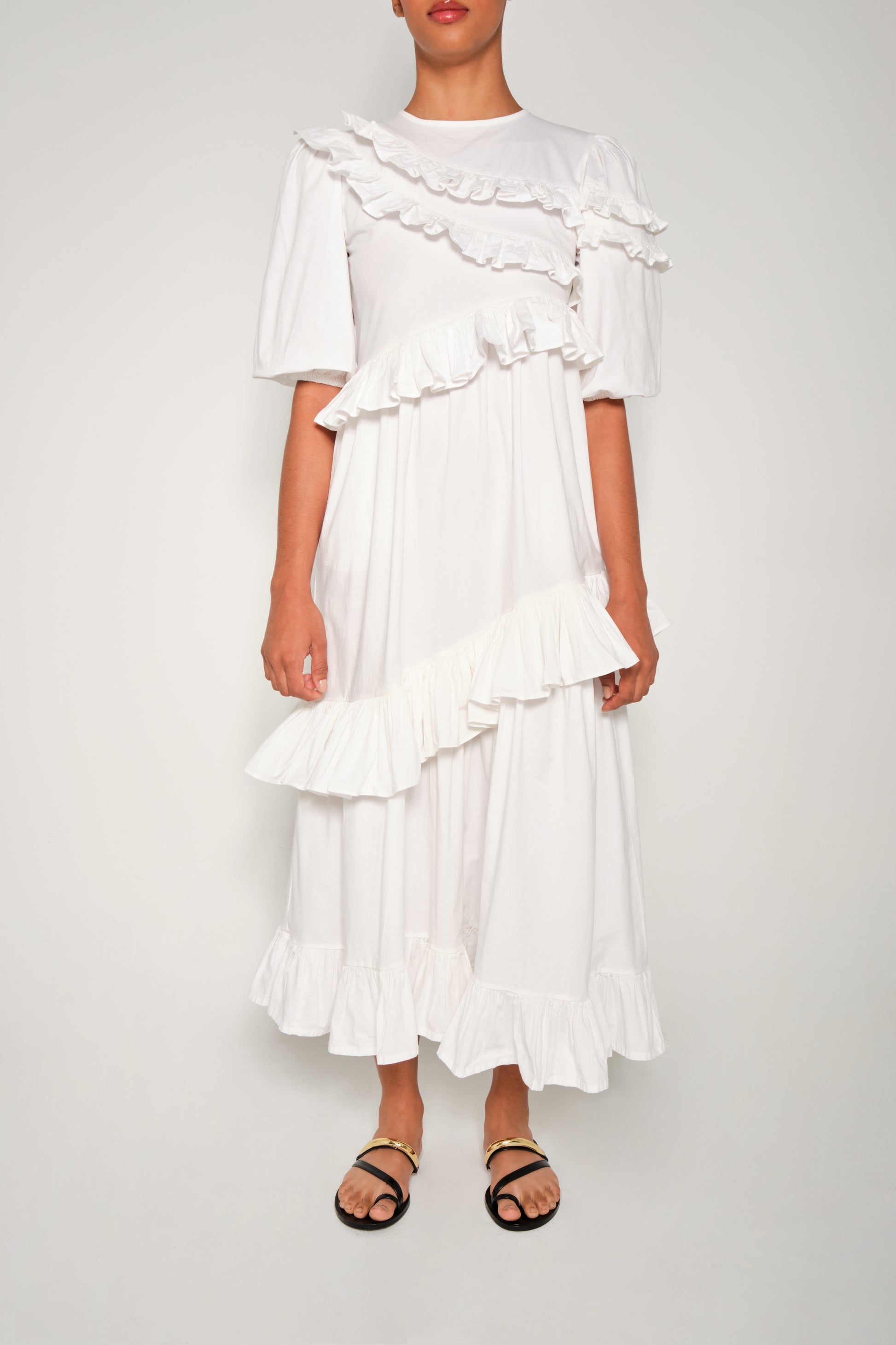 Model wearing white ruffle tiered poplin dress with puff sleeves and asymmetrical skirt.