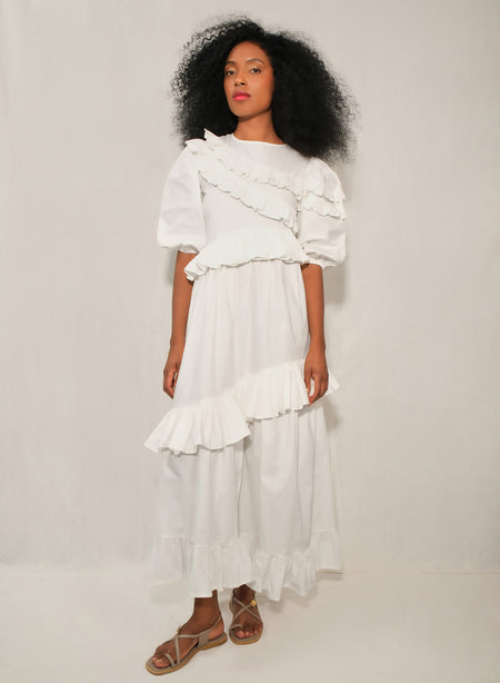 Model wearing white ruffle tiered poplin dress with puff sleeves and asymmetrical skirt.