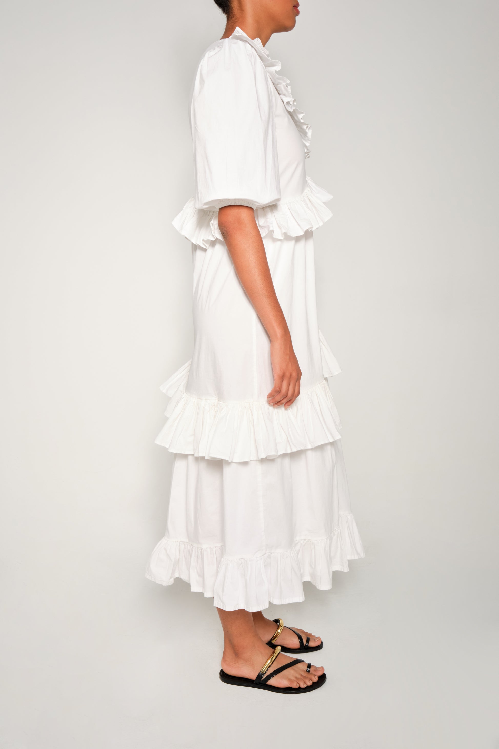 Model wearing white ruffle tiered poplin dress with puff sleeves and asymmetrical skirt.