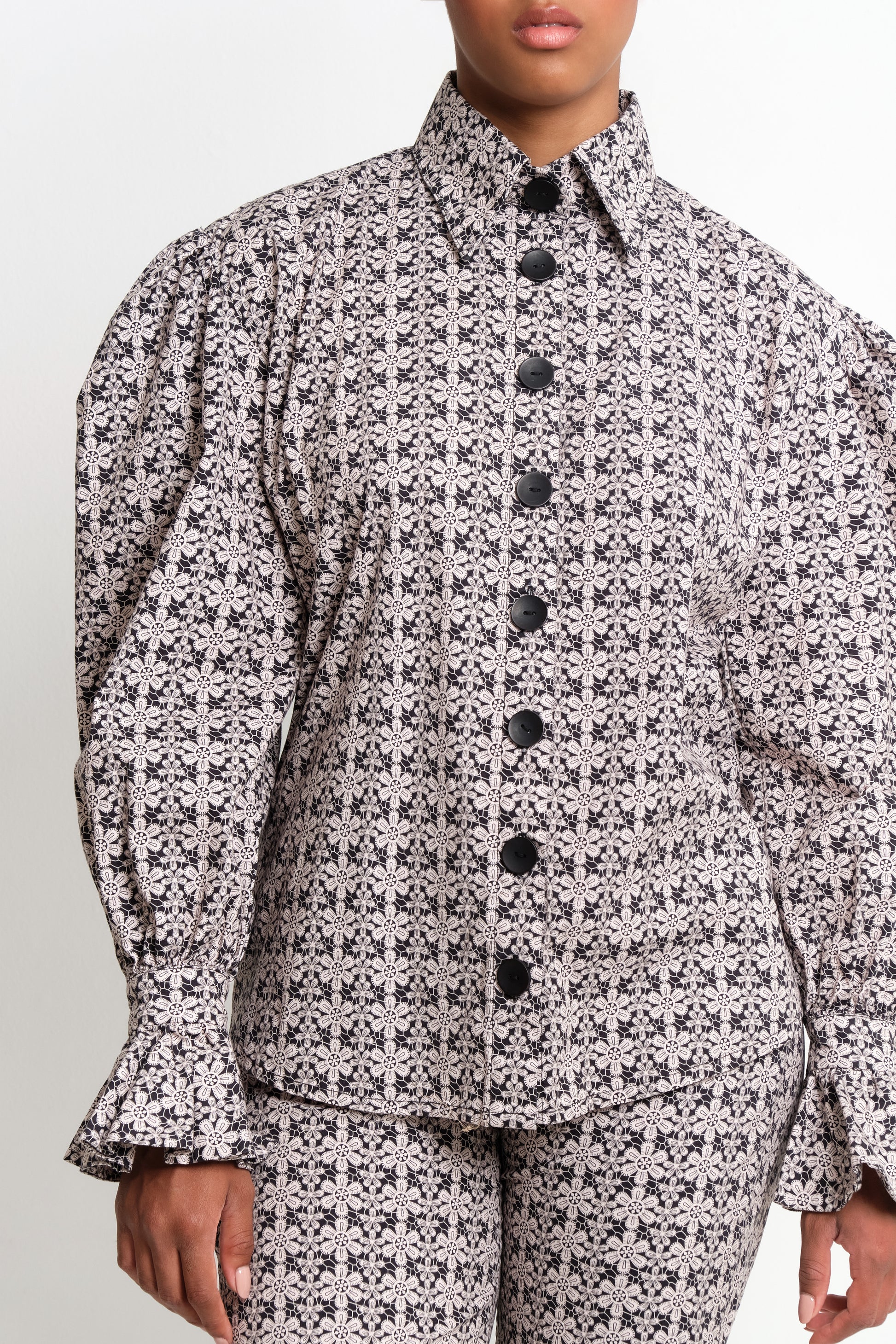 Model in macramé print poplin shirt with puff sleeves and flared ruffle cuffs.
