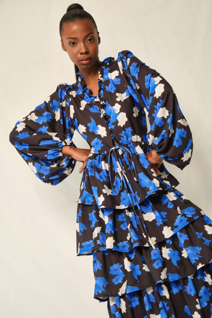 Model wearing tiered maxi dress in Jacaranda print with ruffled V-neckline and balloon sleeves, recycled crepe.