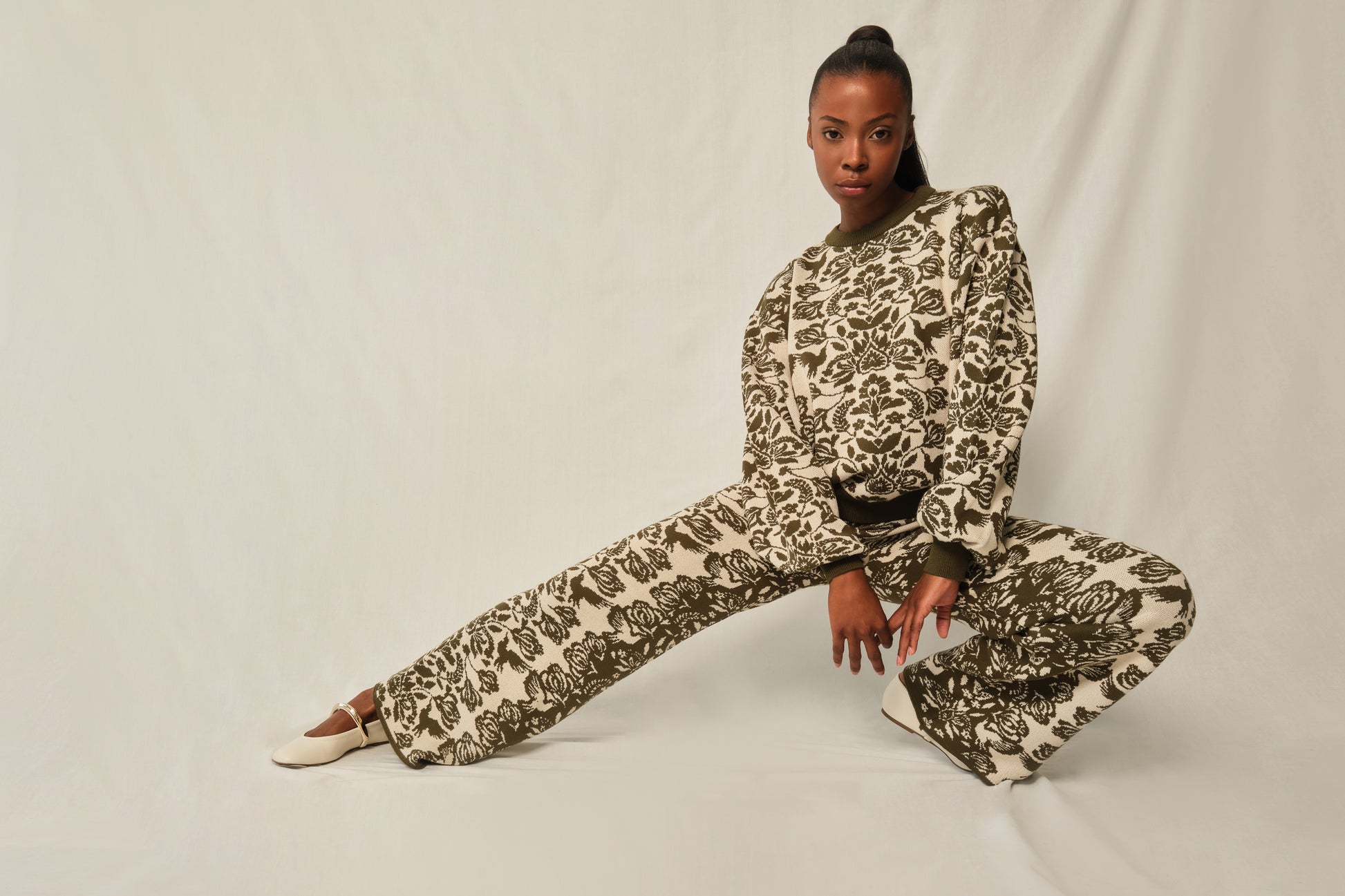 Person wearing a patterned outfit sitting on a white background